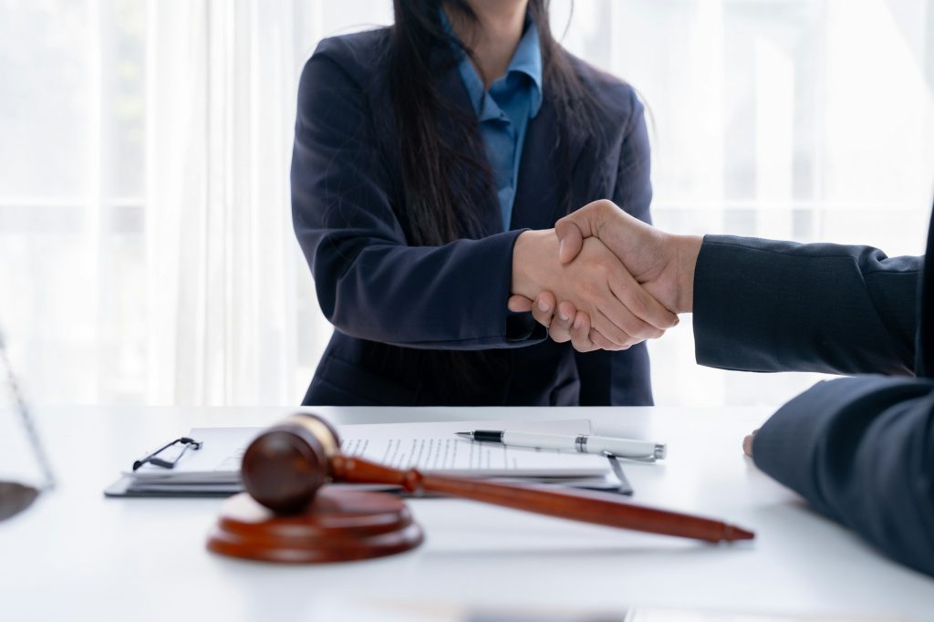 Two professionals shaking hands over a desk with legal documents.